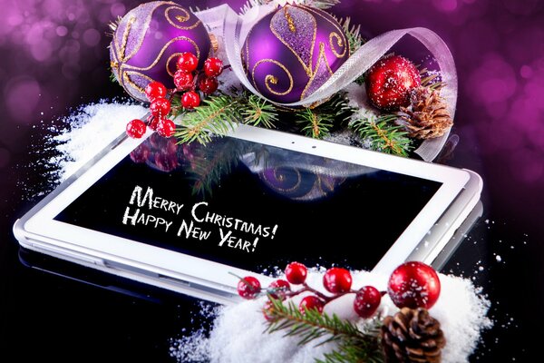 Biały tablet z życzeniami Szczęśliwego Nowego Roku i Bożego Narodzenia fioletowymi bombkami noworocznymi z małymi stosami śniegu z zielonymi gałęziami choinkowymi z szyszkami i czerwonymi jagodami na ciemnym tle