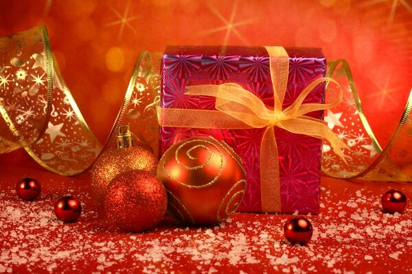 Рождественский подарок в красной обертке с бантом с елочными украшениями и золотой праздничной лентой