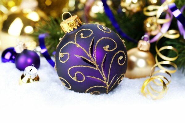 Boule de Noël pourpre dans la neige sous la branche de sapin