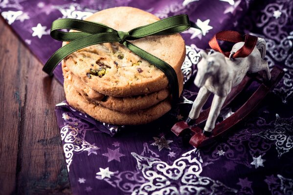 Three cookies in a green ribbon lie on a purple cloth with a horse