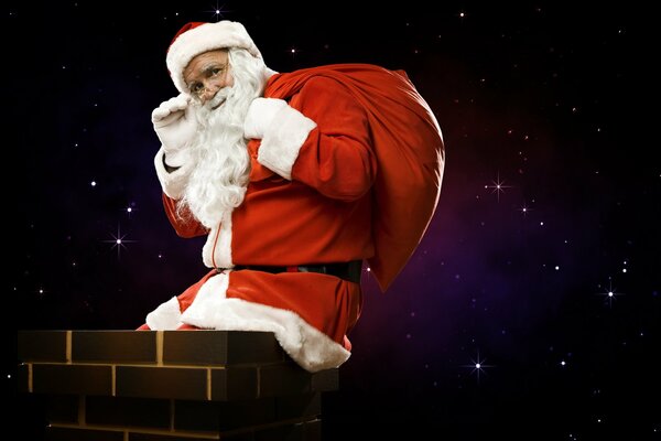 Приветственно махающий рукой и улыбащийся Санта Клаус с мешком подарков сидит на трубе