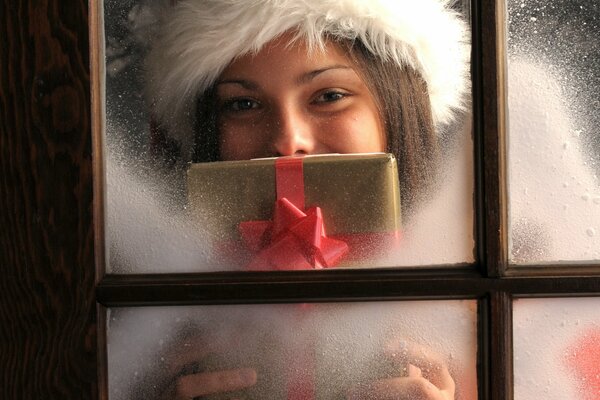 Ragazza in un cappello e con un regalo in mano, guardando fuori dalla finestra