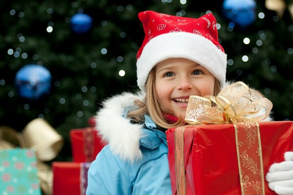 Ein Mädchen in einer Weihnachtsmütze hält ein Geschenk