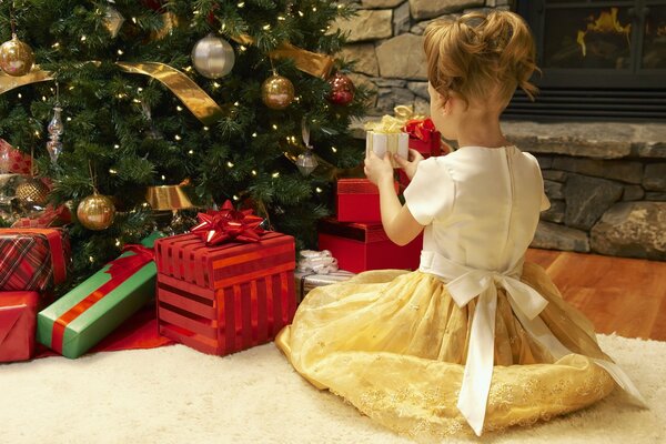 A girl in a dress with gifts near the Christmas tree