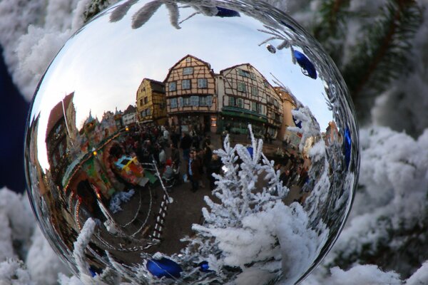 Reflejo de la hermosa ciudad en la bola de año nuevo en el árbol de Navidad cubierto de nieve