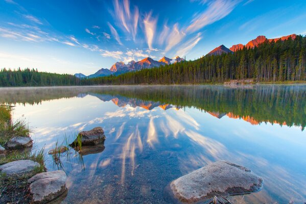 La superficie del lago riflette le montagne e le nuvole del tramonto