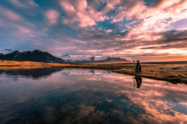 Fotógrafo en la orilla del lago toma una puesta de sol en las montañas