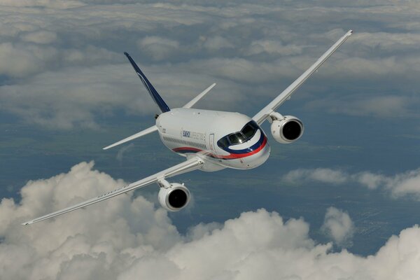 Flugzeug trockener Superjet 100 fliegt vor einem Hintergrund von Wolken