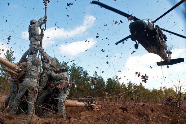 Soldiers mount a gun on the background of a helicopter