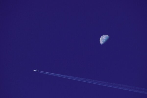 Ein Passagierflugzeug am Himmel, das am Mond vorbeifährt, hinterlässt eine invertierte Spur