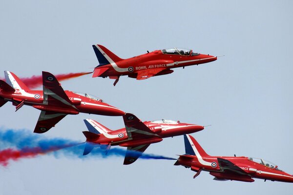 Sur fond de ciel dégagé, des avions rouges libèrent de la fumée multicolore