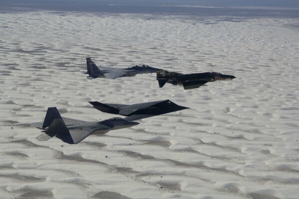 A matte black wedge of fighters over the white sands of the desert