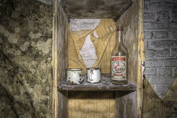 Eine Flasche Wodka und zwei alte Becher im Regal