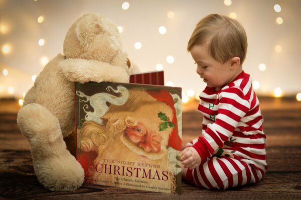 A child in striped pajamas reads a book and sits with a toy