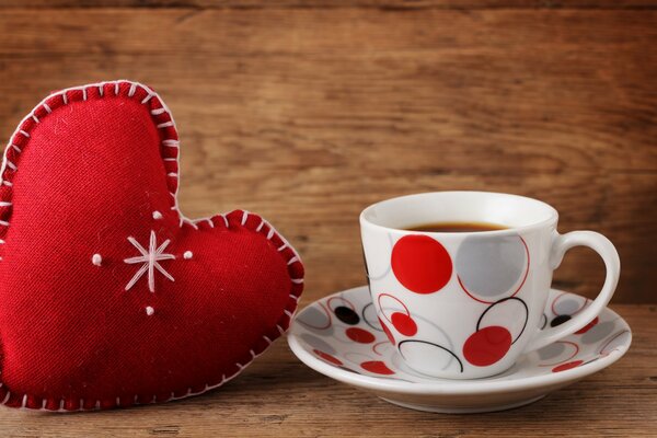 A heart made of cloth next to a mug on a saucer