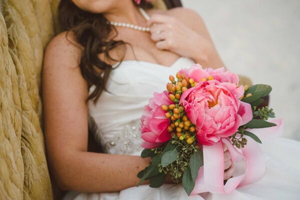 La mariée tient dans ses mains un bouquet de pivoines