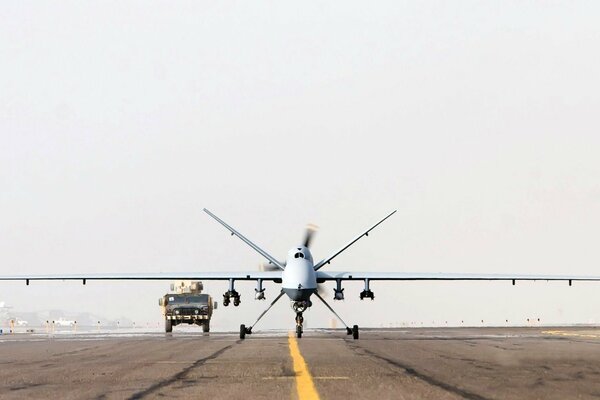 A powerful drone on the runway accompanied by a military vehicle