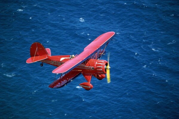 Red biplane flying over the sea