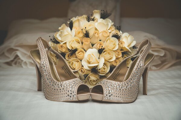 A bouquet of roses on the bed and a pair of beautiful shoes
