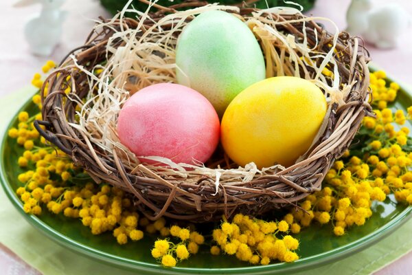 Tres huevos de Pascua en una cesta y una Mimosa