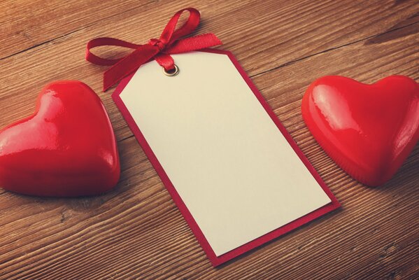 A sign with a red bow and two red hearts on a wooden table