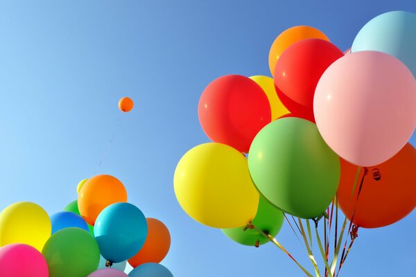 Zwei Bündel von bunten festlichen Luftballons vor dem Hintergrund des blauen Himmels und eine Kugel in der Ferne