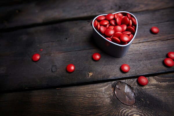 Dragées rouges dans une tasse en aluminium en forme de coeur sur une table en bois