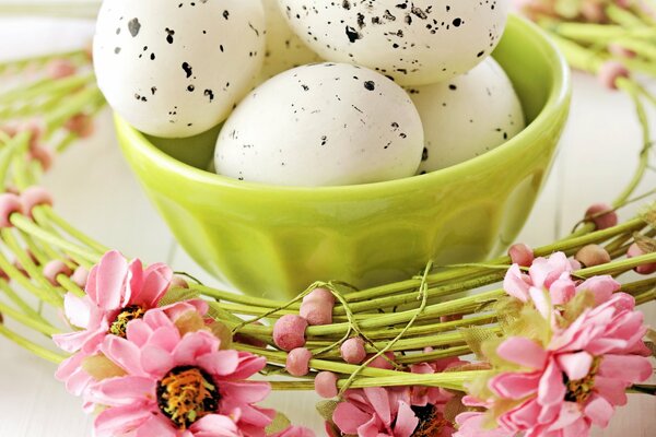 Marble Easter eggs in a light green bowl on the background of a wreath of pink flowers