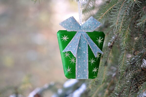 A small gift in a green package is hanging on the Christmas tree