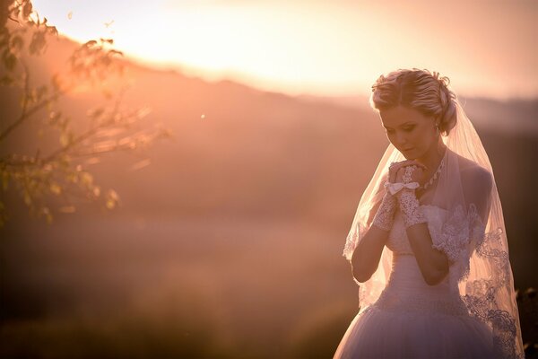 La novia en un velo en el fondo de una puesta de sol