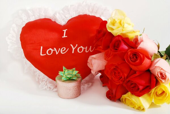 A heart-shaped pillow, a bouquet of roses and a small box decorated with a ribbon