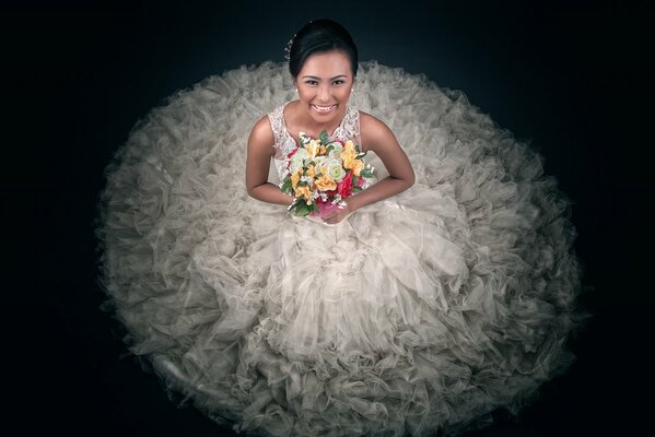 La novia en un vestido exuberante con un ramo sobre un fondo negro