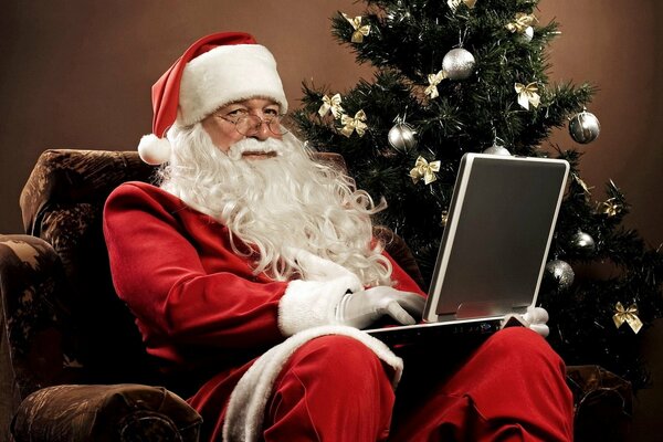 Père Noël dans une chaise avec un ordinateur portable