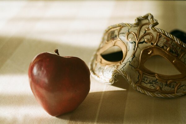 Máscara de carnaval y gran manzana roja a la sombra de la habitación