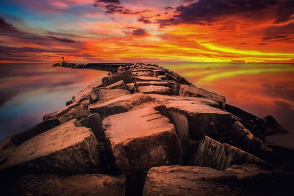 A bright red dawn over the sea among which the breakwater stretches