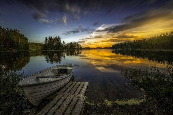Spiegelreflexion der Farben des Sonnenuntergangs am See. Boot an der Brücke