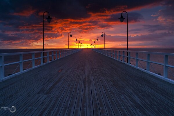 Un largo muelle se aleja donde se ve la puesta de sol