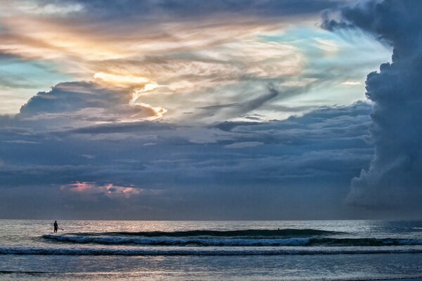 Un hombre junto al mar bajo un enorme cielo