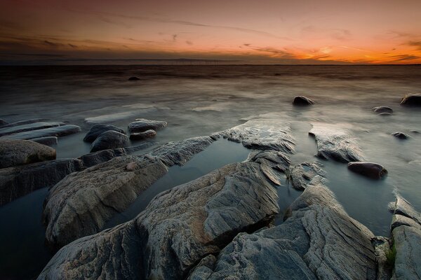 Felsiger Strand vor dem Hintergrund eines orangefarbenen Sonnenuntergangs