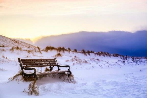 A bench in the snow and footprints around it