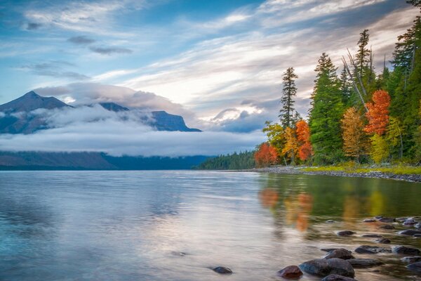 The mountains in the clouds and the forest are reflected in the lake