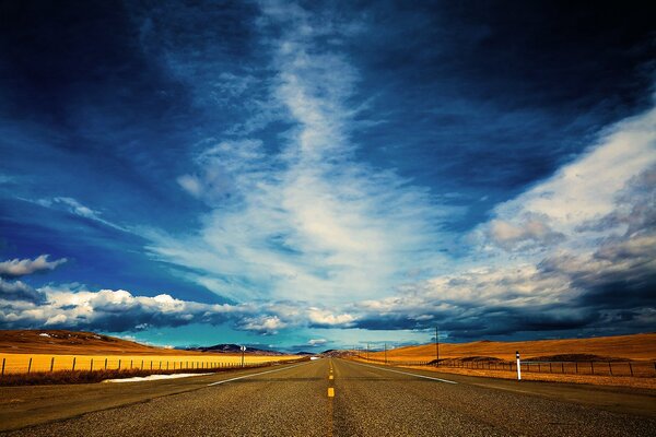 A boundless road with a yellow field and a cloudy sky