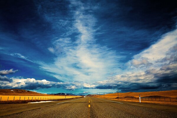 Бескрайняя дорога с желтым полем и облачным небом
