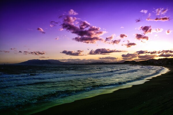 Tramonto lilla sulla spiaggia che lascia le onde a riva