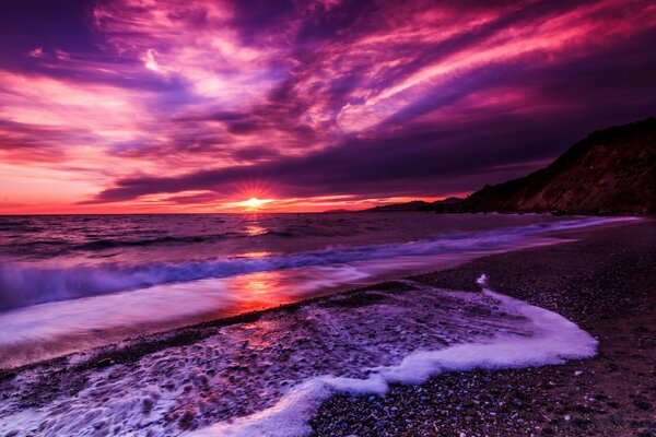 Tramonto lilla e onda con schiuma sulla spiaggia