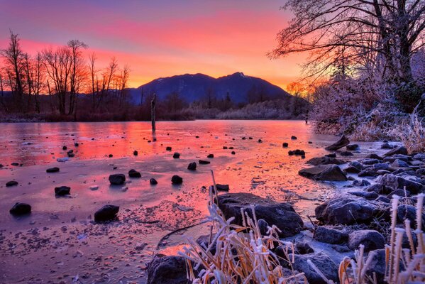 Winter, Sonnenuntergang in den Bergen. Bäume am Fluss mit Steinen