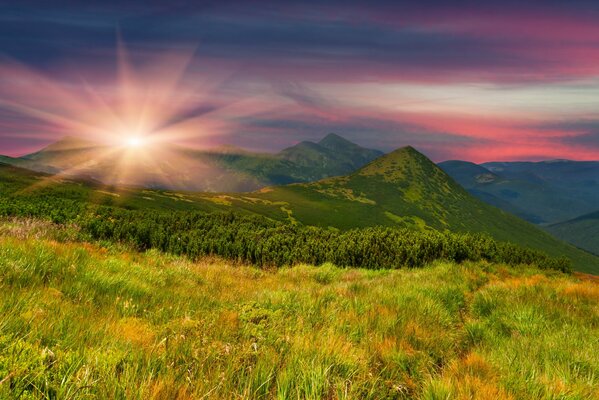 Strahlende Sonne bei Sonnenuntergang vor dem Hintergrund der Berghänge