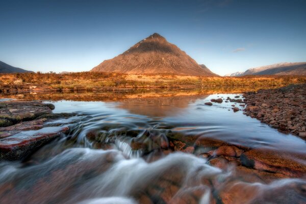 A fast stream, a rocky shore, a mountain in the distance