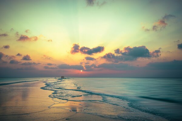 Hermosa puesta de sol escarlata en el fondo de una pareja caminando en la playa