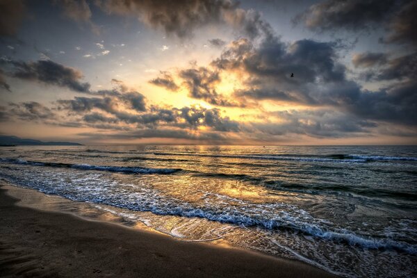 Mer avec les vagues et le sable au coucher du soleil